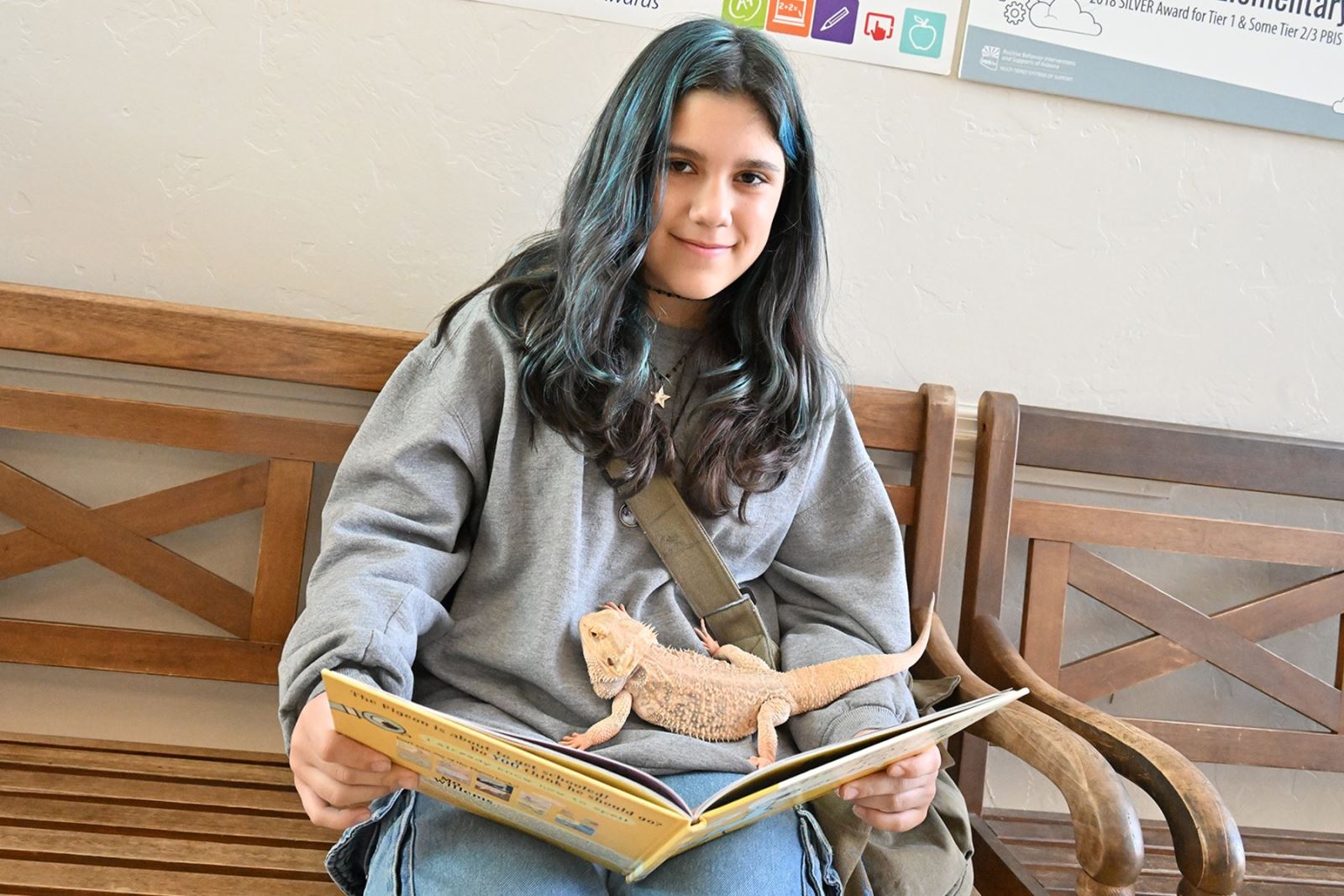 A girl holds Mr. Spikes the bearded dragon, while reading him a book